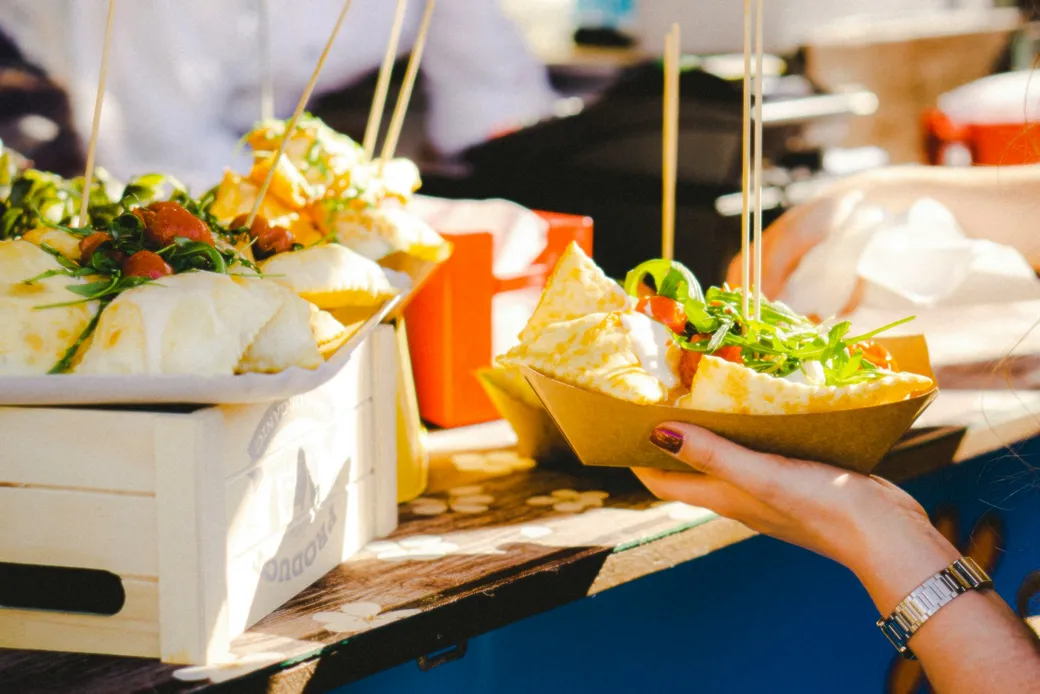 A portion of dumplings, tomatoes and salad in a paper bowl at a food stall counter