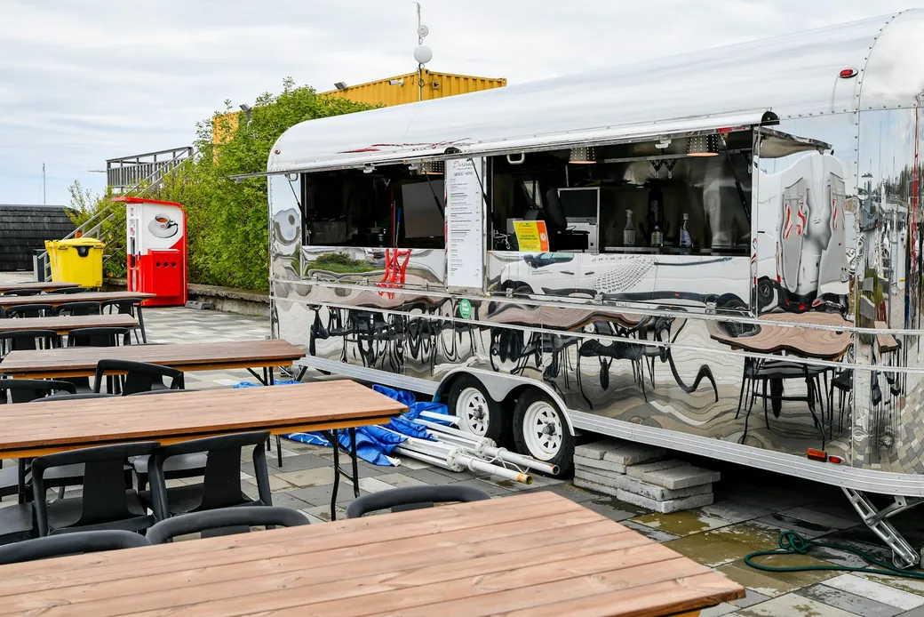 Foodtrailer mit geöffneter Verkaufsklappe und Sitzplätzen im Außenbereich